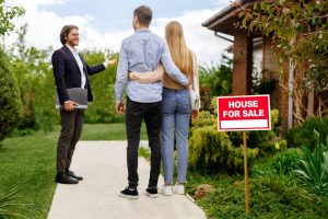 real estate broker showing house for sale to young couple outside