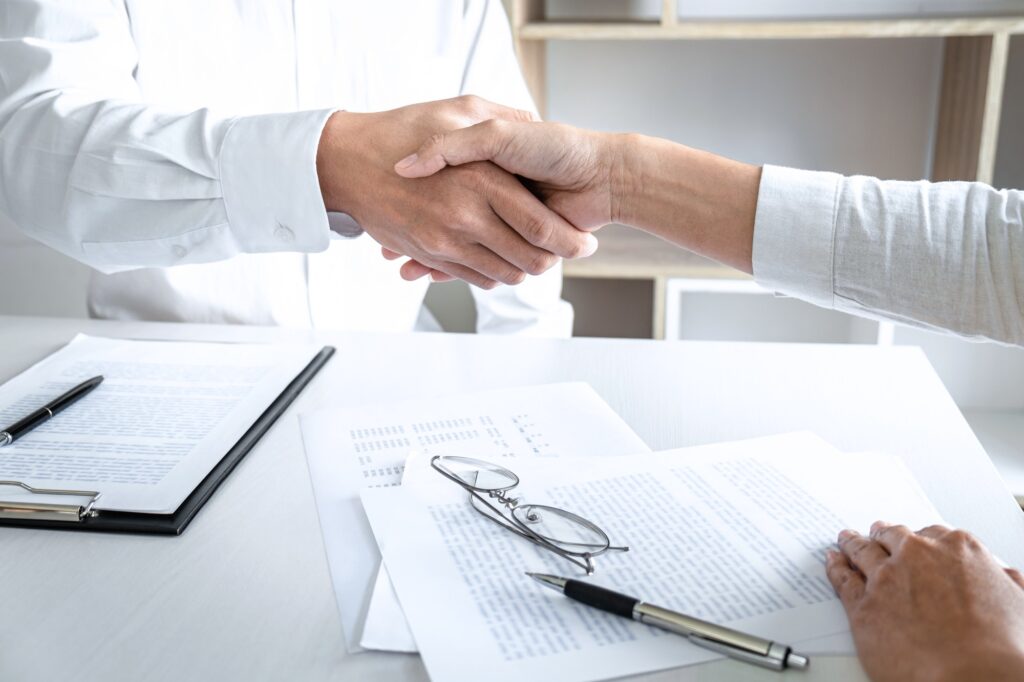 Real estate broker agent and customer shaking hands after signing contract documents for realty